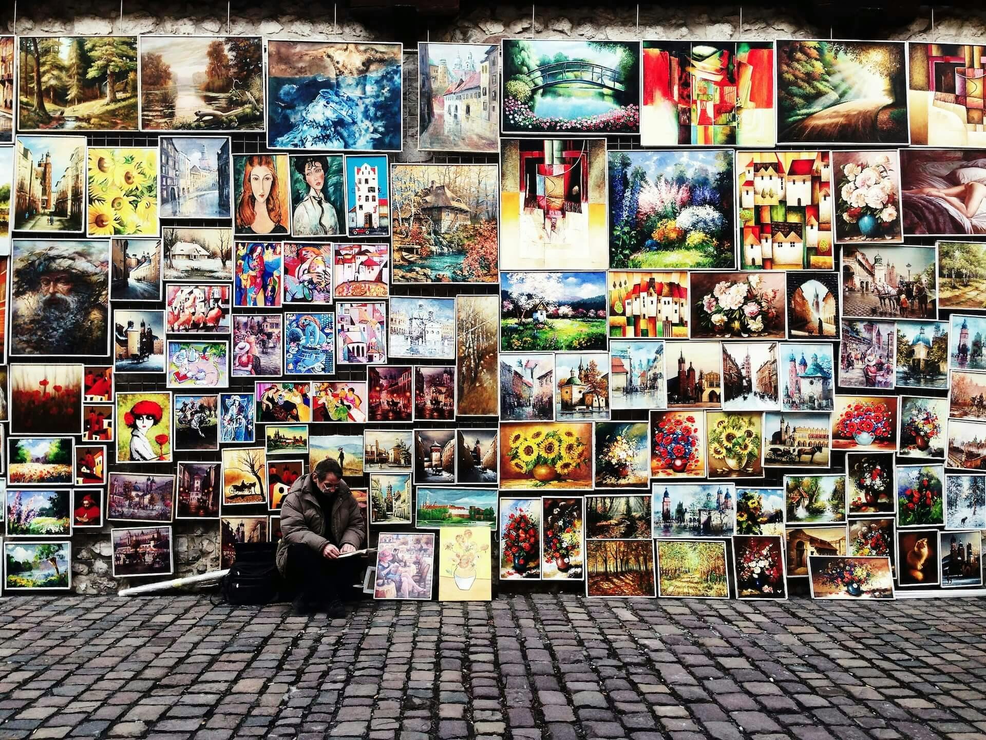 muitas pinturas coloridas em uma parede na rua, na calçada o autor das obras sentado